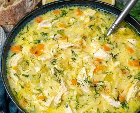 Bowl of creamy Avgolemono soup garnished with lemon and herbs.